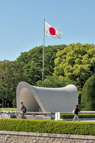 A saddle-shaped monument with trees and the Japanese flag in the background