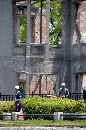 A landscaping crew trims bushes in front of the Atomic Bomb Dome