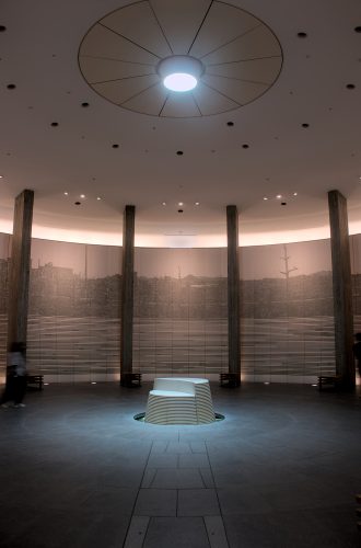 A circular, stone hall with soft lighting and a stone monument in the center under a spotlight