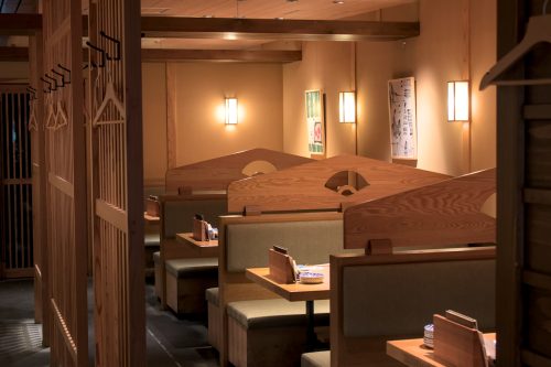 A closeup of the four booths inside Tempura Suehiro showing soft lighting, moss green bench cushions and rich toned wood.