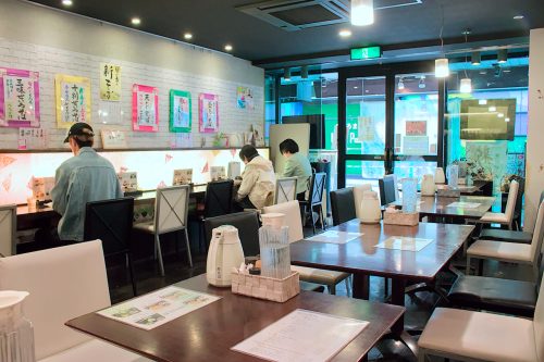 Tightly clustered tables along one side of the shop with a bar on the opposite side and an aisle in the middle