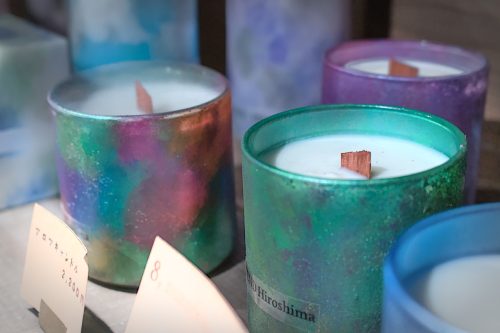 A shelf display of wood-wicked, white-wax candles in iridescent, metallic holders