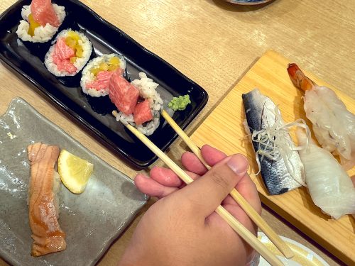 A hand with chopsticks picks up a makizushi roll at Nonta Sushi in Hiroshima City