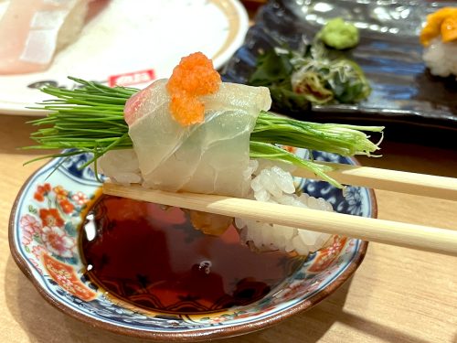 A nigiri sushi held with chopsticks over a dish of soy sauce at Nonta Sushi in Hiroshima City