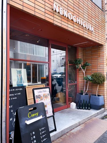 Small, potted trees and signs outside the glass store-front of Nekochigura in Hiroshima