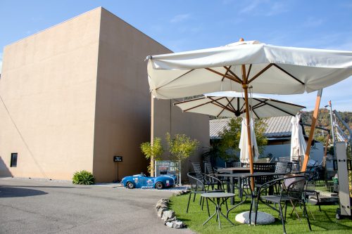 A three story, sand-colored cube beside an astroturf lawn filled with tables, lawn-chairs and patio umbrellas