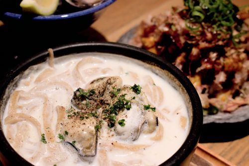 A black stone bowl filled with thick pasta submerged in a deep cream sauce and topped with oysters.