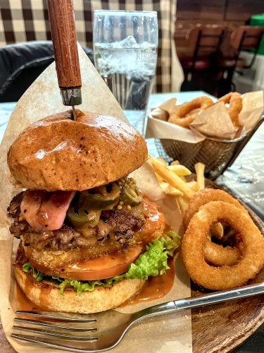 A thick burger with lots of toppings held together with a knife in the top