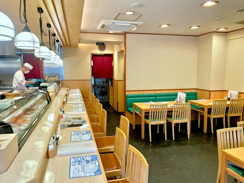 Green upholstered booth chairs and a long bar with a sushi chef at work behind it