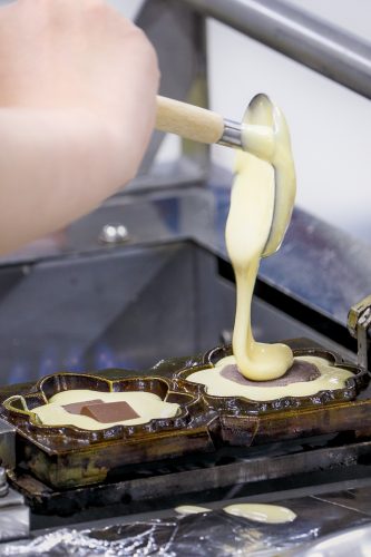 Batter being spooned into a maple leaf-shaped iron
