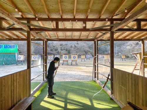 A man in a covered, wooden shelter with archery targets beyond him