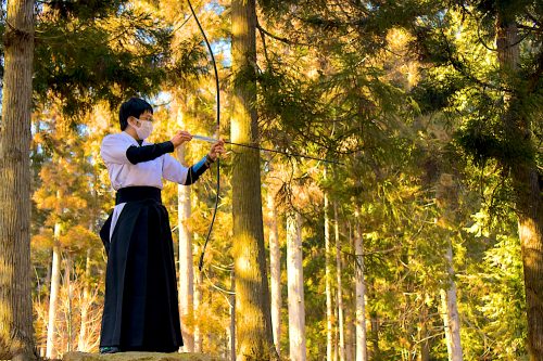 A man in hakama and kimono practices Kyūdo in a golden wood