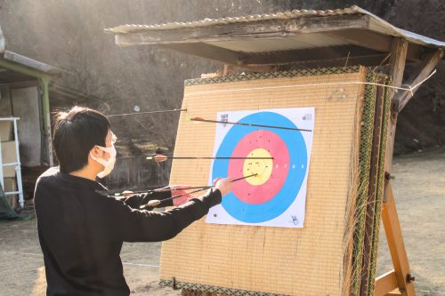 A man removing his arrows from a target paper against a tatami stand