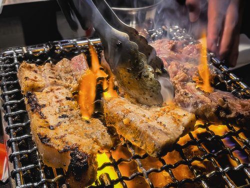 Korean cuts of pork cooking on a barbecue amid flames
