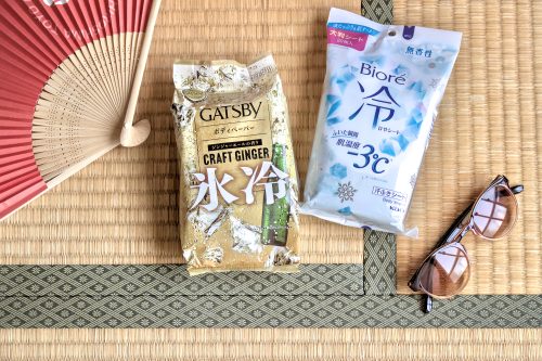 Plastic packages on a tatami mat with a pair of sunglasses in one corner and a folding paper fan in the opposite corner
