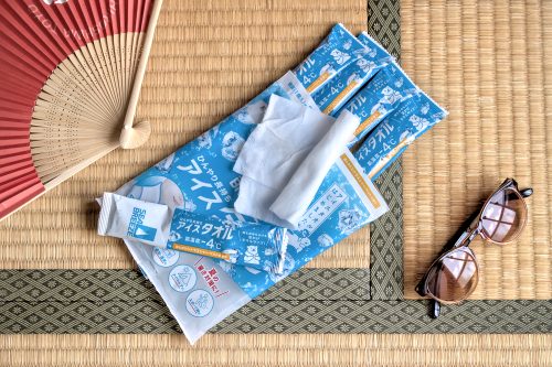 Long plastic packages on a tatami mat with a pair of sunglasses in one corner and a folding paper fan in the opposite corner