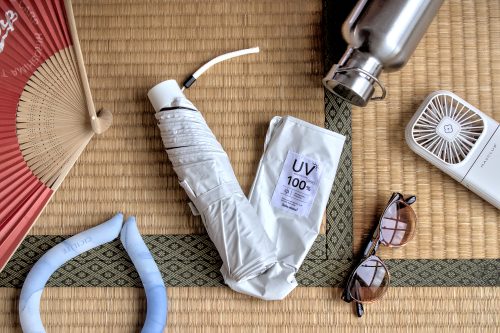 A small, white umbrella wrapped up and lying on its sheath over a tatami mat and surrounded by summer items..