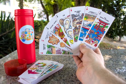 A hand holds seven long playing cards, each one decorated with different Hiroshima themes.