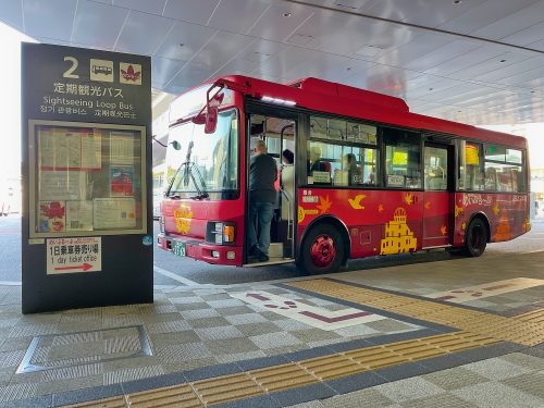 A red bus decorated with yellow Hiroshima tourist sites waits for passengers to get on