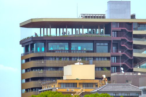 A tall office building with lots of glass windows and a covered observation deck on the top with people looking out the windows