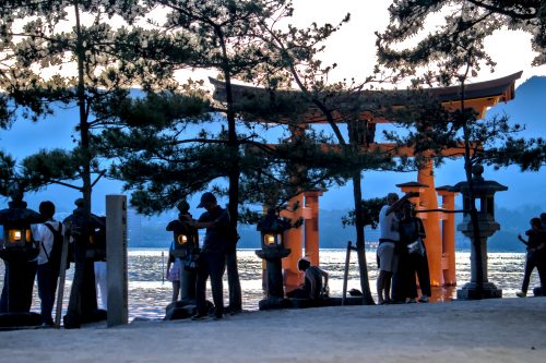 The shapes of tourists take selfies with a large, vermillion Shinto gate