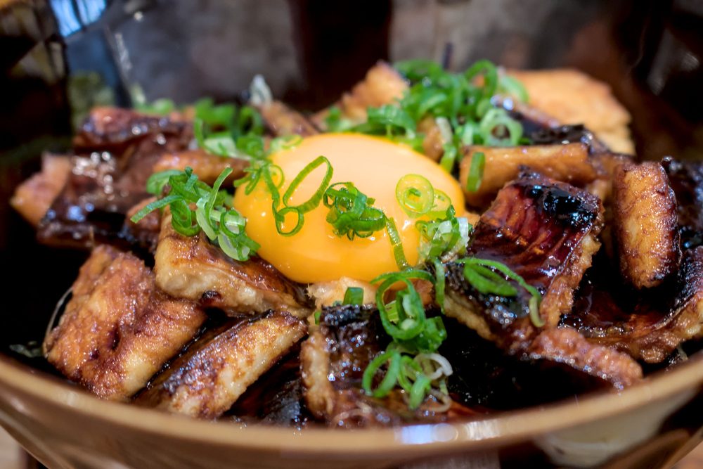A raw egg-yolk atop chunks of grilled conger eel sprinkled with chopped green onions